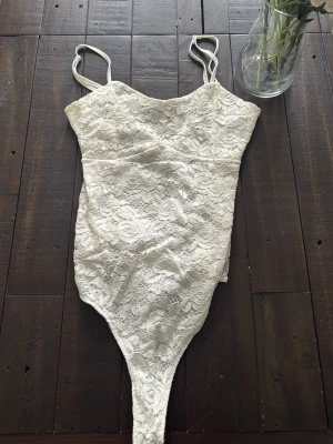 Vit spetsbody med tunna axelband - Snygg vit body i spets med tunna justerbara axelband. Spetsig fram och bak till, men baktill är den transparant (sista bilden), vilket gör den ännu snyggare!😍storlek S men passar även M.