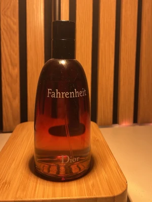 Fahrenheit parfym från Dior - Fahrenheit från Dior är en ikonisk parfym i en elegant glasflaska med en snygg röd till orange gradient och svart kork. Flaskan har tydlig logga framtill och ger ett lyxigt intryck, perfekt för dig som gillar klassiska dofter. Den är nästan helt ny aldrigt använd.