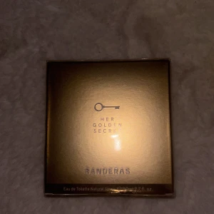 Her Golden Secret parfym Banderas - Her Golden Secret från Banderas är en Eau de Toilette i en lyxig, guldig fyrkantig förpackning med elegant nyckelmotiv på framsidan. Förpackningen har en metallisk finish och text i silver. Perfekt för dig som gillar exklusiva och moderna dofter.