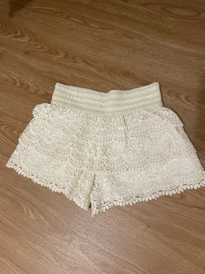 Vita virkade shorts med spetsdetaljer - Säljer ett par vita virkade shorts med bred resår i midjan och fina spetsdetaljer. 
