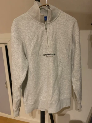 Grå halvzip sweatshirt Jack & Jones - Ljusgrå sweatshirt från Jack & Jones Originals med halv dragkedja och hög krage. Tröjan har trycket 'original Studio' på bröstet och är gjord i mjukt sweatshirtmaterial. Perfekt för en avslappnad och stilren look. Hör av dig vid minsta fundering och pris kan självklart dikskuteras! 💯🙌