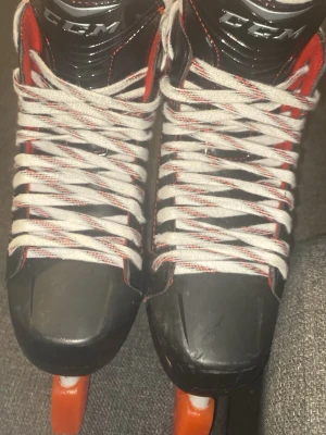 Svarta CCM hockeyrör med röda detaljer - Säljer ett par svarta hockeyrör från CCM med röda och vita detaljer. Skorna har vita snören och en robust plastkonstruktion med röd insida. Perfekta för dig som gillar att åka skridskor och vill ha en sportig look.
