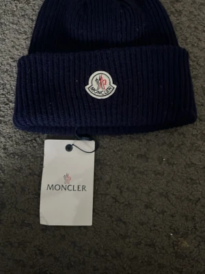 Mörkblå ribbstickad Moncler mössa - Priset kan diskuteras 😁.Säljer en mörkblå ribbstickad mössa från Moncler med uppvikt kant och klassisk Moncler-logga framtill. Mössan är tillverkad i mjukt material och har en stilren, tidlös design som passar perfekt till höst och vinter. Tveka inte med att skriva för minsta fråga 😁