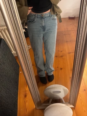 Ljusblå raka jeans - Säljer ett par ljusblå jeans med rak passform och klassisk femficksdesign. Jeansen har hög midja och stängs med knapp och dragkedja. Perfekta för en avslappnad och trendig look. Waist 27, längd 30