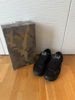 Svarta Valentino Garavani sneakers - Säljer ett par Snygga svarta sneakers från Valentino. Skick 8/10 litet hål se bild 4. Säljer pga sugen på nytt, använt cirka 1 år. Får med box och dustbag