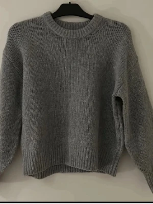 Grå stickad tröja med rund hals - Mysig grå stickad tröja med rund halsringning och långa ärmar. Den har ganska bra skick enda saken är att den har lite få små rosa fläckar pga färg vid halsringningen men kan kanske gå bort vid tvätt vet ej