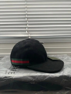 Svart Gucci keps med GG-mönster - Går att beställa våran Snygg svart keps från Gucci med klassiskt GG-monogram över hela kepsen. På sidan finns en grön och röd rand som ger den där ikoniska Gucci-looken. För andra typer av kepsar kontakta mig, många olika modeller kan fixas. Beställning blir billigare 💫
