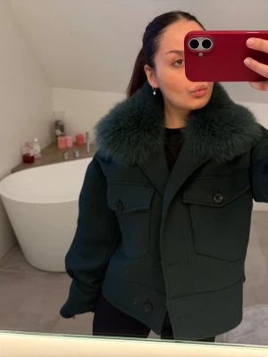 Meotine pälsjacka  - Säljer en mörkgrön pälsjacka från Meotine med stor fluffig krage i matchande färg. Jackan har inga defekter alls. Den har två stora bröstfickor med knappar och en kort, boxig passform. Perfekt för dig som vill ha en trendig och varm vinterjacka med snygga detaljer. Pris går att diskutera💚💚