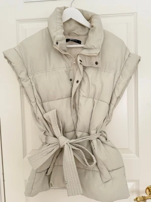 Beige väst med knytband - Kommer ej till användning! Beige väst med knytband dessutom finns både knappar och dragkedja. 