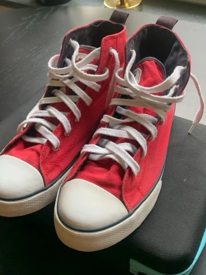 Polo Ralph Lauren Röda höga sneakers, strl 40 - Snygga röda sneakers i canvas med vita gummisulor och tåhättor. Skorna har vita skosnören och svarta innerfoder. Klassisk high-top modell som passar perfekt till jeans eller shorts. Inga synliga loggor eller märken. Använda men i väldigt bra skick 