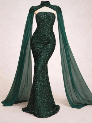Mörkgrön glittrig långklänning - Säljer en magisk mörkgrön långklänning med glittriga paljetter och dramatiska, transparenta släp som fästs vid axlarna. Klänningen har en unik cut-out vid halsen och markerad midja för en elegant siluett. Perfekt för bal eller festkvällar.