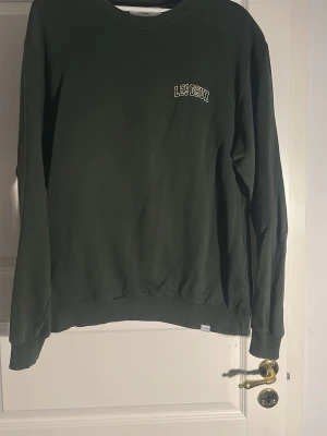 Mörkgrön sweatshirt från Les Deux - Mörkgrön sweatshirt från Les Deux med rund halsringning och diskret logga broderad på bröstet. Tröjan har långa ärmar, ribbade muddar vid ärmslut och nederkant. Tillverkad i mjukt bomullsmaterial som är skönt att bära.