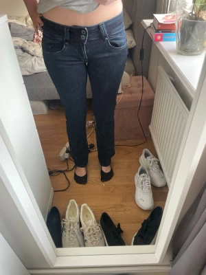 Mörkblå slim fit jeans med dubbla knappar - Säljer ett par mörkblå slim fit jeans med dubbla knappar i midjan och klassiska fem fickor. Jeansen har en snygg tvätt och raka ben. Perfekta för dig som gillar en enkel men stilren look.