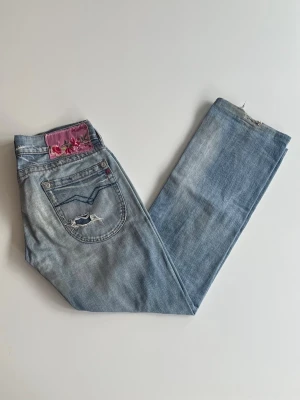 Ljusblå slitna replay jeans  - Säljer ett par ljusblå jeans med slitningar på knäna och bakfickan. Jeansen har en rak passform och en snygg broderad detalj med blommor på bakfickan. Modell: WV 470 färg: 032, producerade tidigt 2000 tal. 