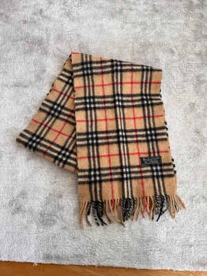 Rutig halsduk Burberry - Säljer en klassisk beige halsduk från Burberry med det ikoniska rutiga mönstret i svart, vitt och rött. Halsduken är tillverkad i 100% lammull. Säljer för 499kr. Hör av er om ni har frågor eller funderingar😃