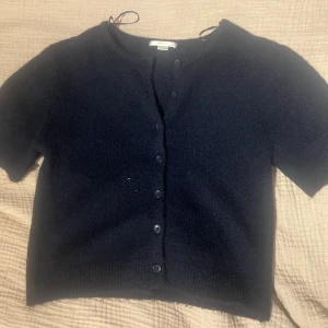 Svart kortärmad kofta med knappar  - Mysig svart kofta med korta ärmar frpn gina tricot. Koftan har knäppning framtill med flera svarta knappar och är stickad i ett mjukt material. Perfekt att slänga över en topp för en enkel och stilren look. Passar xs/s. Ny pris 229 💓