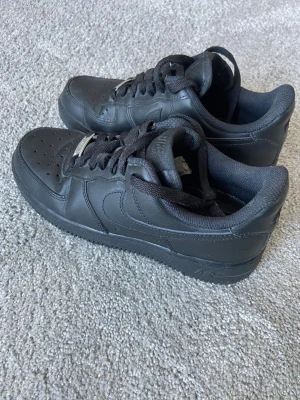 Svarta Nike Air Force 1 sneakers - Klassiska helsvarta Nike Air Force 1 sneakers. Använda endast en gång så dom är nästintill i nyskick.