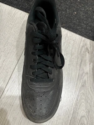 Helvita svarta sneakers med snörning - Snygga helsvarta sneakers med klassisk låg profil och snörning. Ovandelen är i slätt läderliknande material med perforeringar på tån för ventilation. Tjock svart sula och vadderad plös för extra komfort. Passar perfekt till streetwear och casual outfits.