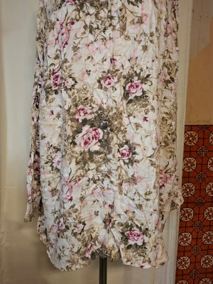 Blommig blusaktig från Cellbes - Charmig blommig blusaktig från Cellbes i mjuka toner av rosa och grönt. Blusen har en romantisk känsla med sitt vackra blommönster och är perfekt för vår och sommar. Den har en bekväm passform och är tillverkad i ett lätt material.