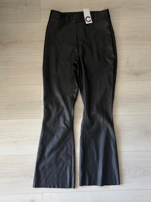 Svarta coated leggings med utsvängda ben - Snygga svarta leggings med coated yta och utsvängda ben från märket C. Hög midja och stretchigt material som ger en cool look. Perfekta att styla med en oversized tröja eller crop top.