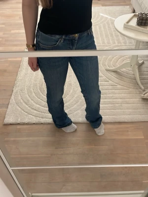 Blå bootcut jeans med låg midja - Säljer ett par klassiska blå bootcut jeans med låg midja och fem fickor. Jeansen har en snygg tvätt och subtila slitningar för en avslappnad look. Passar perfekt till både sneakers och boots. Stängs med dragkedja och knapp framtill. Skriv gärna vid funderingar!❤️