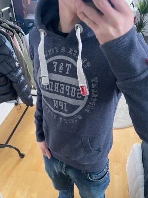Vintage 2000s Superdry Hoodie (sällsynt) - Snygg mörkblå hoodie från Superdry med stort vitt tryck på bröstet och vita ränder på ärmarna. Hoodien har en stor huva med vita dragsnören och ribbade muddar. Perfekt för en avslappnad streetwear-look. Storlek S men passar XS bättre! Skriv vid funderingar 📲🤝