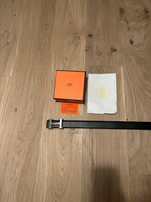 Svart hm bälte i skinn - Snyggt svart hm bälte med en hm logga i silverfärg. Tillverkat i exklusivt skinn och levereras med originalask och dustbag. Perfekt accessoar för att lyfta vilken outfit som helst.