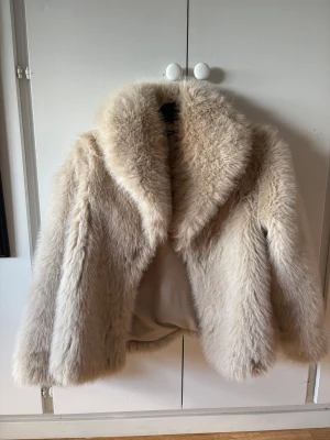 Beige pälsjacka från Gina Tricot - Säljer en fluffig beige pälsjacka från Gina Tricot i storlek XS. Jackan har bred krage, mjukt foder och en riktigt lyxig känsla. Perfekt för att hålla värmen under kalla vinterdagar. Stängs framtill i en hake och har en klassisk, rak passform. 