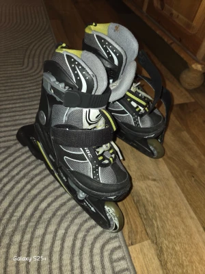 Svarta och gråa inlines med gula detaljer - Säljer ett par svarta och gråa inlines med gula detaljer och vita inslag. De har justerbara spännen och kardborreband för bra passform. Hjul och stomme i plast och metall. Perfekta för dig som gillar att åka inlines utomhus.