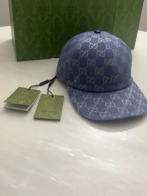 Dubai navy blå GG keps  - Säljer en blå keps från GG med det klassiska GG-monogrammet i vitt över hela kepsen. Kepsen har böjd skärm och är tillverkad i ett slitstarkt tyg som ger en exklusiv känsla. Perfekt för dig som vill ha en trendig accessoar med lyxig touch.