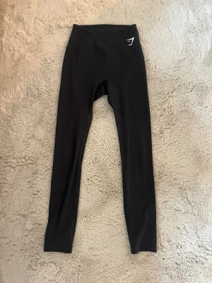 Mörkgrå leggings från Gymshark - Säljer ett par mörkgrå leggings från Gymshark med stretchigt material. Diskret logga i vitt på höften. Vet inte storleken men skulle säga typ S
