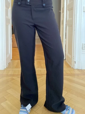 Svarta vida kostymbyxor - Snygga svarta kostymbyxor med vida ben. Byxorna har dubbla knappar framtill. Perfekta för en stilren look och passar till många olika outfits. Materialet är mjukt och följsamt.