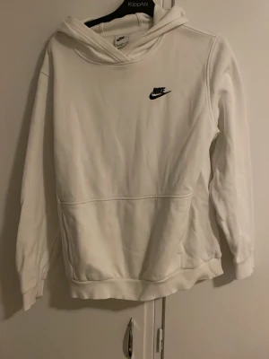 Vit hoodie från Nike med logga - Snygg vit hoodie från Nike med svart broderad logga på bröstet. Klassisk känguruficka framtill och ribbade muddar vid ärmslut och nederkant. Tillverkad i mjukt material och har en stor huva för extra komfort.
