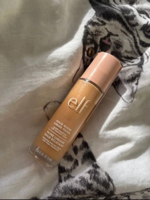 e.l.f. Halo Glow Liquid Filter foundation - Säljer en e.l.f. Halo Glow Liquid Filter foundation i en varm beige nyans. Kommer i en genomskinlig glasflaska med persikofärgat lock och pump. Ger glowig finish och kan användas både som foundation eller highlighter. Perfekt för dig som vill ha naturlig lyster.