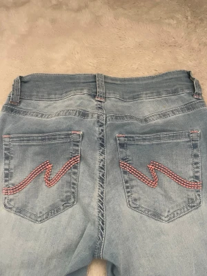 Ljusblå bootcut jeans från Nelly  - Säljer ett par ljusblå bootcut jeans med snygg rosa broderad detalj på bakfickorna från Nelly . Super stretchiga och sköna, storlek 36. Skriv gärna om du vill ha en bättre bild på dom!