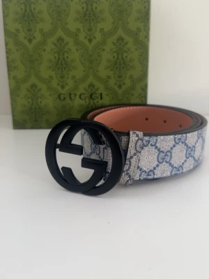 Gucci GG Supreme bälte blå/vit - Snyggt Gucci GG Supreme bälte med blått och vitt monogrammönster och stor svart GG-logga som spänne. Bältet är gjort i skinn med klassisk design och exklusiv känsla. Perfekt accessoar för att lyfta din outfit.