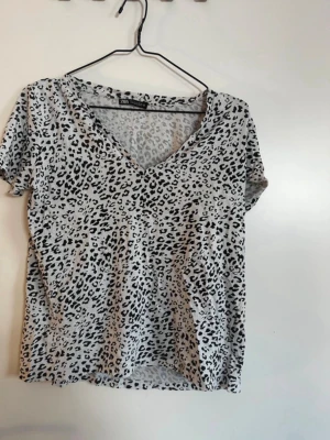 Leopardmönstrad t-shirt från Zara - Snygg t-shirt från Zara med leopardmönster i svart och grått. T-shirten har v-ringning och korta ärmar, perfekt för dig som vill sticka ut lite extra. Tillverkad i mjuk bomull som känns skön mot huden. Rök och djurfritt hem. Pruta gärna !🌸
