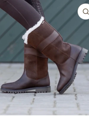 Bruna fodrade ridstövlar - Snygga bruna ridstövlar med grov sula och vitt foder. Stövlarna har en mix av slätt och mockaliknande material samt dekorativa sömmar. Perfekta för kalla dagar och ger en sportig look.