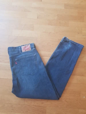 Levi's blå 505 raka jeans - Klassiska blå jeans från Levi's med rak passform och fem fickor. Jeansen har den ikoniska röda Levi's-lappen på bakfickan och patch i midjan. Tillverkade i slitstark denim med snygga kontrastsömmar. Perfekta för en avslappnad och tidlös stil.