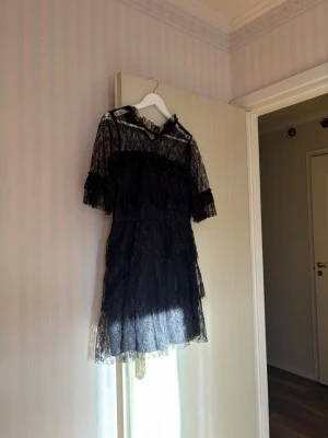 Svart spetsklänning med volang - Snygg svart kortklänning i spets med volangdetaljer. Klänningen har korta ärmar med volang. 