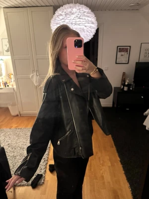 Svart skinnjacka med dragkedjor - Snygg svart skinnjacka i klassisk bikerstil med silvriga dragkedjor och bred krage. Jackan har detaljerade sömmar och fickor med dragkedja framtill. Perfekt för dig som vill ha en edgy och trendig look. Jackan är i mycket bra skick utan defekter.