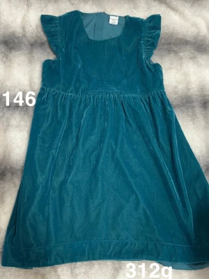 Velour klänning med volangärm - Söt blå/grön klänning i mjuk velour med volangärmar och rund halsringning. Klänningen har en lätt utställd passform och är perfekt för dig som gillar en bekväm men ändå stilren look.🌸 Sparsamt använd. Storlek 146