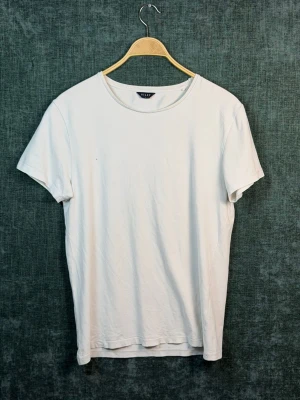 Vit basic t-shirt från Riley - En klassisk vit t-shirt från Riley i storlek L. T-shirten har rund halsringning och korta ärmar, perfekt för en clean och enkel stil. Tillverkad i mjuk bomull som känns skön mot huden. Passar till allt och är ett måste i garderoben.