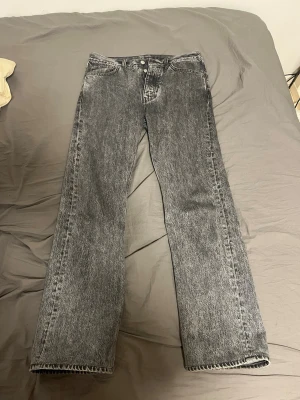 Grå raka jeans med tvättad look - Säljer ett par grå jeans med rak passform och klassisk femficksdesign. Jeansen har en snygg tvättad finish och stängs med knapp och dragkedja. Perfekta för en avslappnad och trendig stil. Modellen heter rush av hope men har blivit ett hål där bak och sytt den ända defekten på jeansen annars ingenting. storlek 29