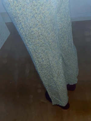 Blommiga pyjamasbyxor med dragsko - Säljer ett par lösa och bekväma pyjamasbyxor med blommigt mönster i ljusgult, blått och vitt. Byxorna har resår i midjan och dragsko för extra komfort. Perfekta för mysiga hemmakvällar och chill dagar.