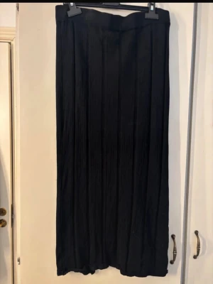 Svart långkjol med plisserad look - Säljer en svart långkjol med plisserad effekt. Kjolen har en rak och enkel design med resår i midjan för skön passform. Perfekt att styla med både sneakers och boots för en trendig look.