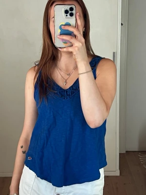 Blå linnetopp från Hollister - Snygg blå linnetopp från Hollister med v-ringning och virkade detaljer vid halsen. Toppen är ärmlös och har en avslappnad passform, perfekt för varma dagar. Liten Hollister-logga nertill på framsidan. Använt den väll men inga fläckar eller defekter. Står som xs men passar S-M skulle jag säga 