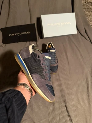 Philippe Model  - Snygga sneakers från Philippe Model i mörkblå mocka och mesh med detaljer i beige och blått på sulan. Klassisk låg modell med vita och blå inslag, samt logga på sidan. Perfekta för dig som gillar stilrena och trendiga skor.