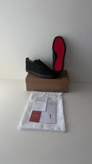 Svarta Christian Louboutin sneakers - Snygga svarta sneakers från Christian Louboutin med klassisk röd sula. Skorna har en låg profil, rund tå och är tillverkade i slätt läder. Kommer med originalpåse och äkthetskort. I bra skick, säljer då jag har skaffat andra skor. Hör av dig vid frågor. 