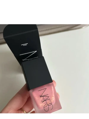 NARS Liquid Blush Orgasm 15ml - Flytande rouge från NARS i nyansen Orgasm, en persikorosa färg med guldskimmer. Kommer i en stilren glasflaska med svart lock och pump. Perfekt för att ge kinderna en fräsch glow och naturlig lyster.